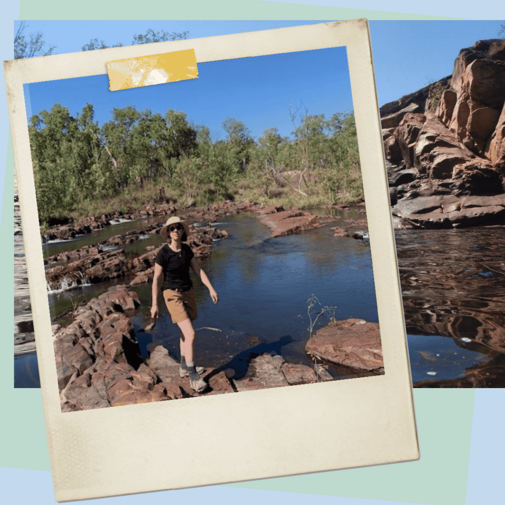 A person wearing a hat, black shirt, and brown shorts walks on rocky terrain by a river with a background of trees and a clear blue sky, captured in a polaroid-style frame overlapping a rocky landscape.