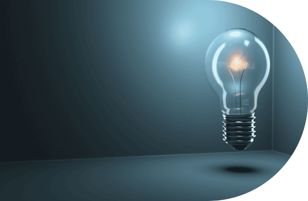 A lit lightbulb floats in a dark, minimalist room with a blue tint. The bulb's filament glows warmly, casting a subtle reflection on the surfaces around it. The background is simple and uncluttered, emphasizing the lightbulb.