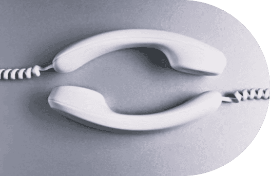 Two white corded telephone handsets are placed facing each other on a gray surface, evoking the supportive connection of a mental health helpline, with their cords extending outward horizontally.