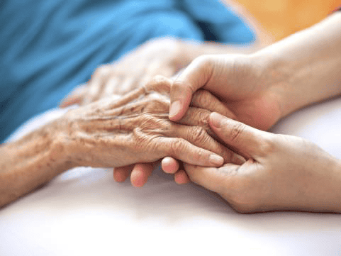 Close-up of a younger person gently holding the hand of an elderly person, conveying care and support—an image that reflects compassionate governance, with both hands resting on a light-colored surface.