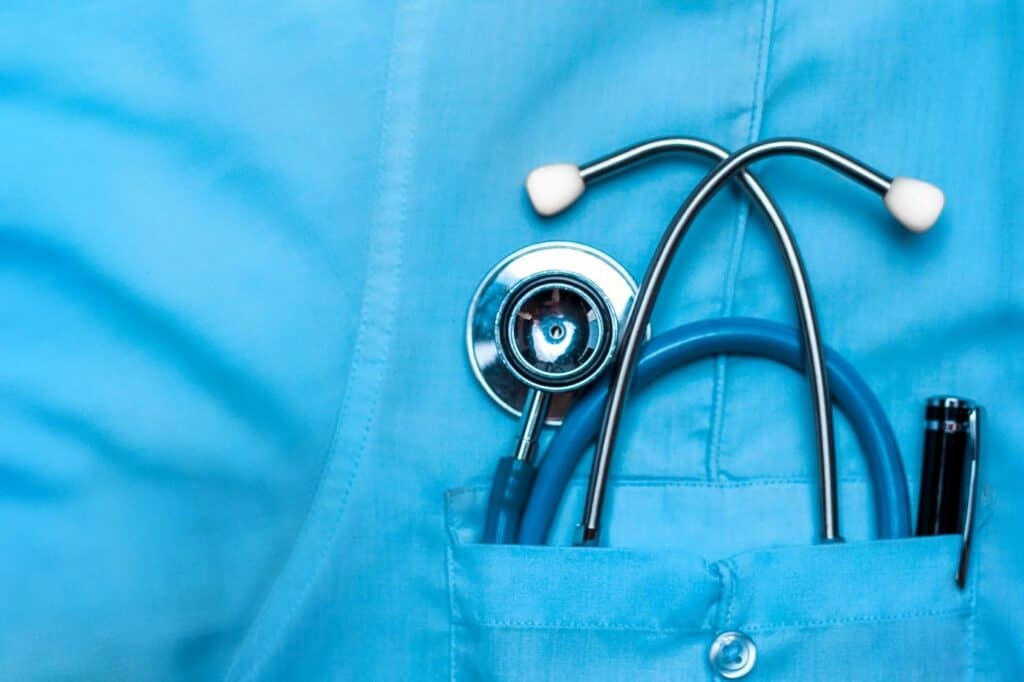 A close-up of a stethoscope and a pen tucked into the chest pocket of a blue medical uniform, symbolizing healthcare in New Zealand and the medical profession.