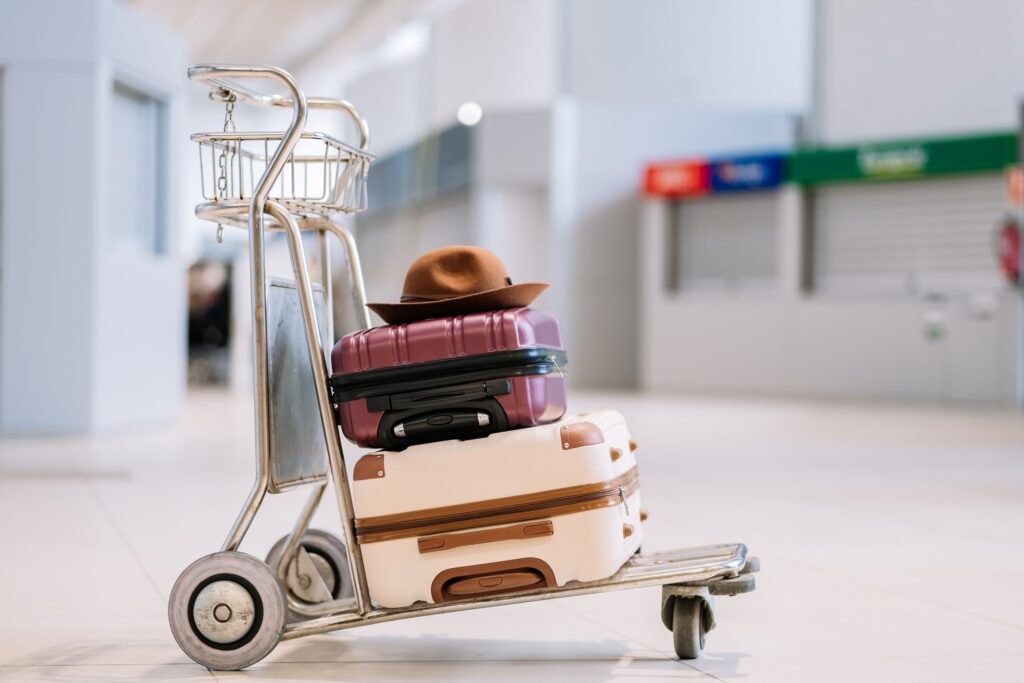 A luggage trolley with a brown hat resting on top, as well as a purple suitcase and a white suitcase, stands alone in an empty airport terminal, subtly representing the economic effects of tourism and emphasising the significance of travel within global tourism economics.